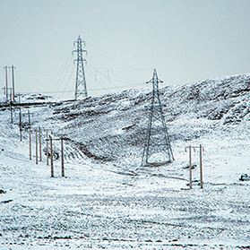 hill side covered in snow with high voltage powerlines spanning up the side