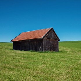Small barn on the side of a plush green grass covered hillside